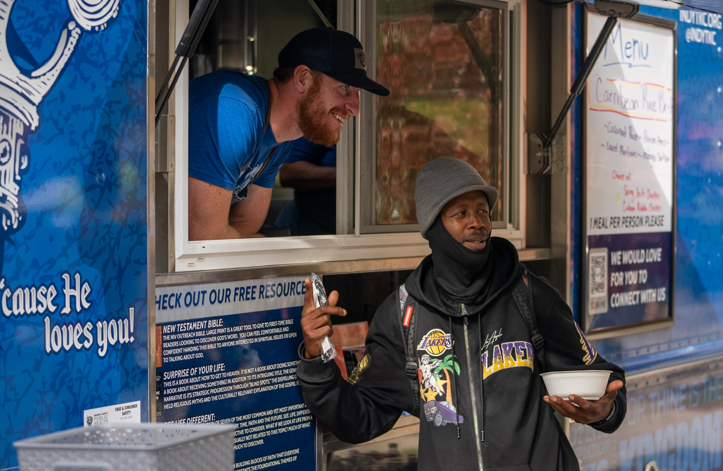 A volunteer from AO1 Foundation's Thy Kingdom Crumb food truck smiles while serving a warm meal to a man in the community.